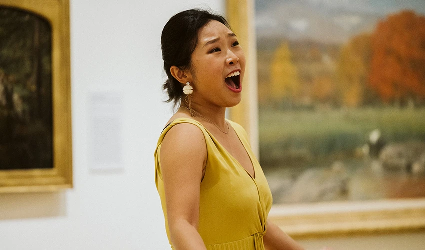photo of a singer in a yellow dress performing in front of a painting
